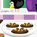 窓辺に鳥がいるキッチンのテーブルには、チョコレートとナッツがトッピングされたクッキーが皿にのっている。