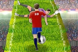 赤いユニフォームのサッカー選手が芝生の上をボールでドリブルし、倒れたゴールキーパーをかわしている場面。