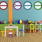 カラフルな室内に円形の窓が並び、子供用の机や椅子、絵画用イーゼル、ボールやおもちゃが床に散らばっている。