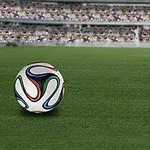 緑のサッカー場の上にカラフルなサッカーボールが置かれ、背景には満員の観客席が広がっている。