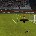 サッカー場で選手がゴールを狙ってボールを蹴り、ゴールキーパーが高台から見守っている様子。