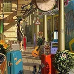 駅のプラットフォームに停車した青と黄色の電車、周囲にはスーツケースや植物、ギターが配置されている。