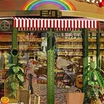 カフェの店先に赤と白のストライプの日よけがあり、ガラス越しに植物やパンが見える。