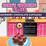 赤い髪のアニメ風キャラクターが指を立てた横に、ラズベリーチョコレートカップケーキがテーブルの上に乗っているキッチンの背景。