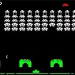 黒い背景に白いエイリアンの隊列と、緑色のシールドが配置されたレトロなアーケードゲーム画面。