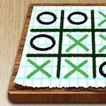 木製の板の上に置かれたマス目の方眼紙に黒い丸と緑のXが描かれている図。