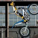 黄色いヘルメットとスーツを着たバイクライダーが、バイクでウィリーして木製の足場を越えようとしている。